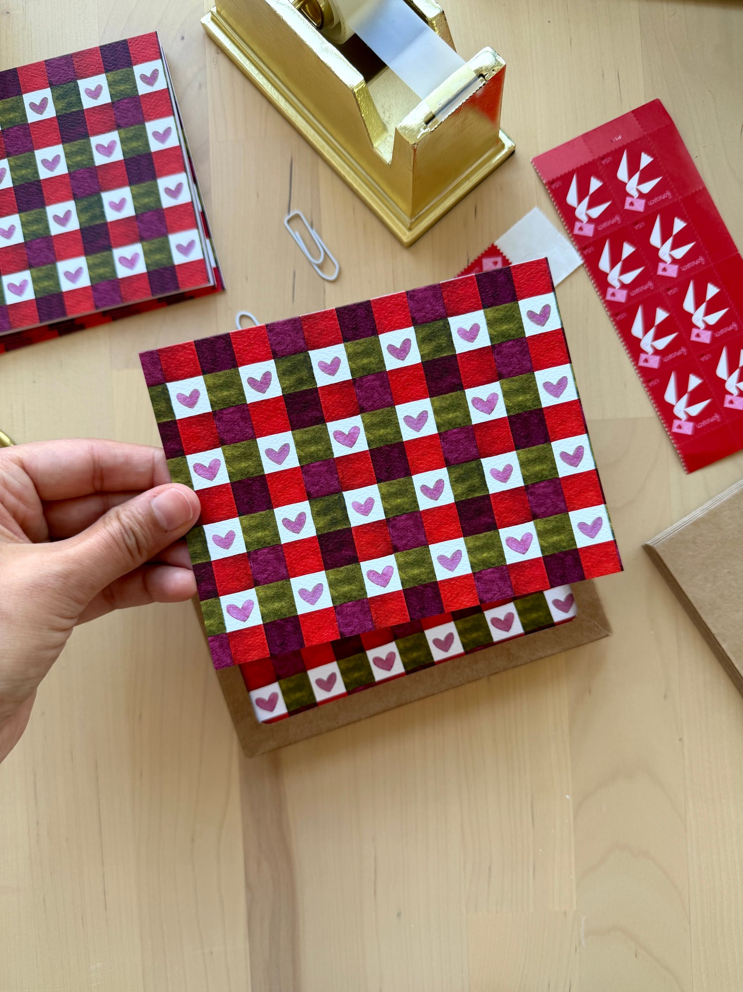 Hand holding a red and green checkered greeting card with heart patterns on writing desk